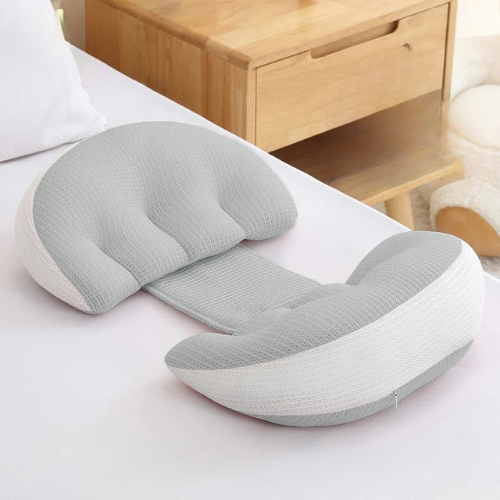 כרית תמיכה בצורת U בצבע אפור ולבן מונחת על מיטה ליד שידת עץ, עם רצועת חיבור מרכזית – מיועדת לתמיכה בבטן או בגב לנשים בהריון.